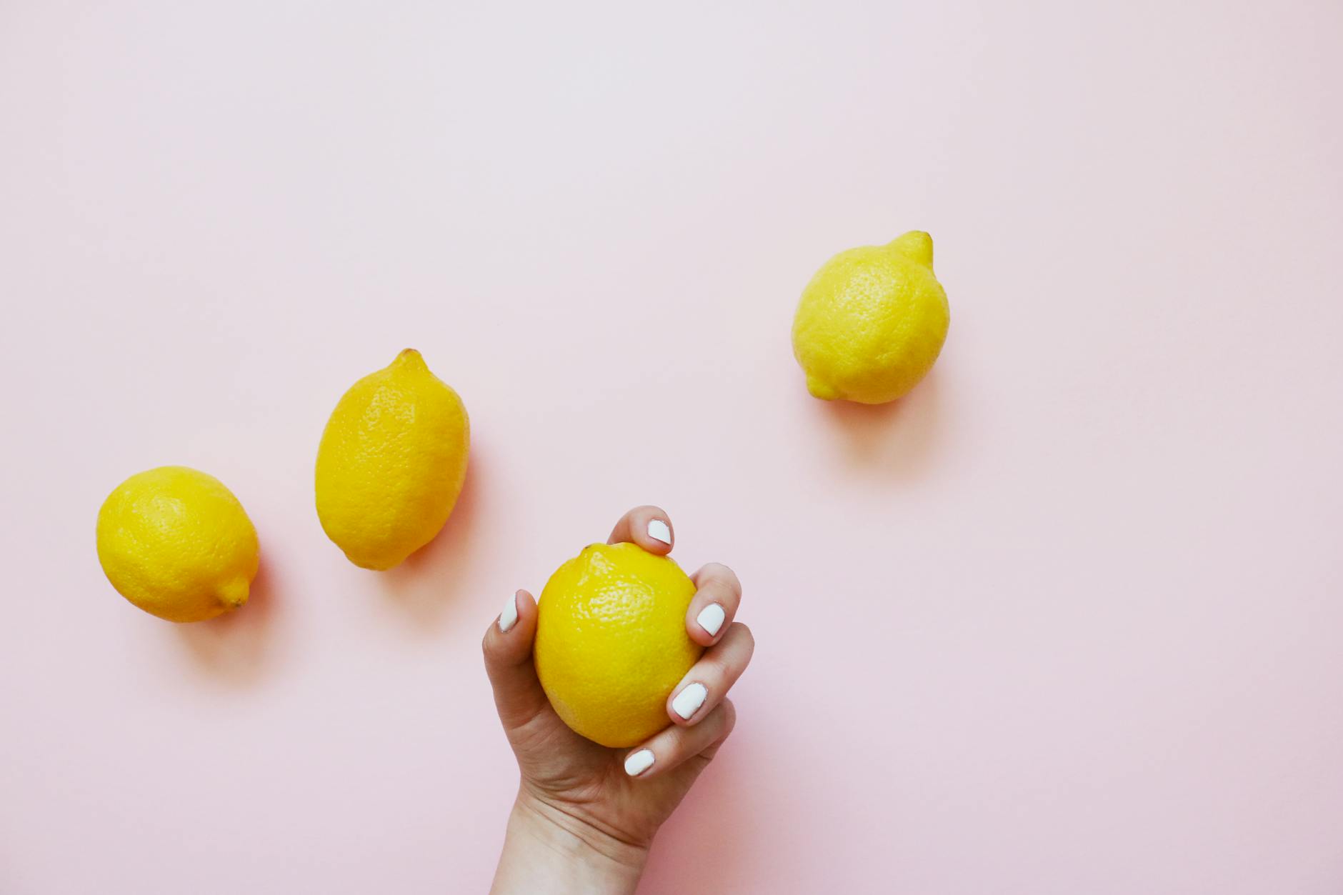 A hand holding a lemon on a soft pink background, symbolizing portable pleasure.