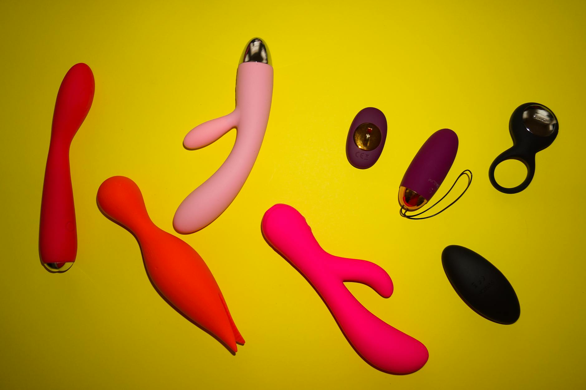 Colorful adult toys arranged on a bright yellow surface, representing choice and comfort in pleasure recovery.